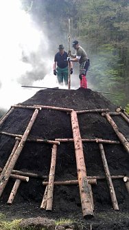 Traditionsk&ouml;hlermeister Otto Ibe und Auszubildender Andr&eacute; Heinz beim Nachf&uuml;llen des Quandelschachts, um einen optimalen Verkohlungsprozess einzuleiten.  (Foto: Forstamt Bleicherode S&uuml;dharz)