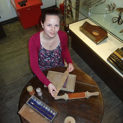 Die Kulturfreiwillige Hanna Messner f&uuml;hrt ein historisches Roll-Brett  (um 1900) zum Pillendrehen vor. (Foto: Museum Tabakspeicher)