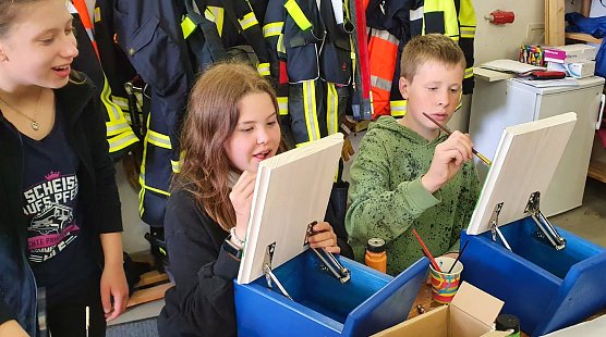 Luisa Rahn, Johanna Bernsdorf und Johann Sch&uuml;tze (v.l.n.r.) von der Jugendfeuerwehr bemalen die Klappen der Stempelk&auml;sten. (Foto: Gabriele Knust)