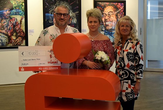 Kundenberaterin Anke Huhn &uuml;berreicht den gl&uuml;cklichen Gewinnern einen symbolischen Scheck und Blumen. (Foto: KSK)