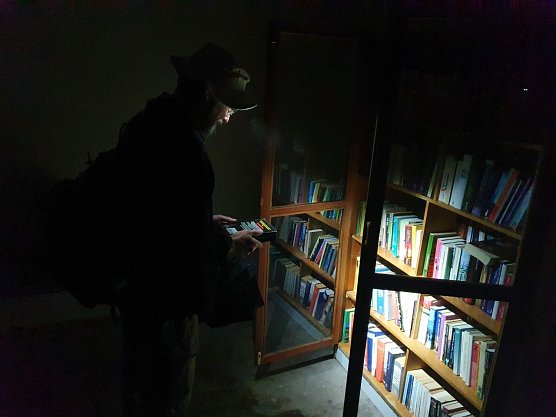 Hier sind wir nicht in eine fremde Wohnstube eingedrungen: In Morungen gibt es eine exklusive Bushaltestelle mit reich gef&uuml;llten B&uuml;cherschr&auml;nken zur kostenlosen Bedienung. Wanderfreund Christian aus Jena l&auml;sst es sich nicht nehmen, im Schein seiner Taschenlampe ein wenig zu st&ouml;bern und schlie&szlig;lich ein Buchexemplar in seinen Rucksack zu stecken.  (Foto: Bodo Schwarzberg)