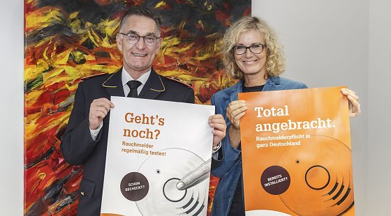 Bild: Hartmut Ziebs, Pr&auml;sident des Deutschen Feuerwehrverbandes (DFV), und Claudia Groetschel, Sprecherin der Initiative Rauchmelder retten Leben stellten gemeinsam die Plakate zum Rauchmeldertag 2017 vor.