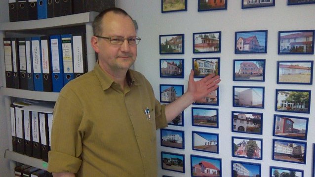 Bild: Ulf Zaspel in seinem B&uuml;ro vor der Wand mit Sehensw&uuml;rdigkeiten von St&auml;dten, die er per Video pr&auml;sentiert
