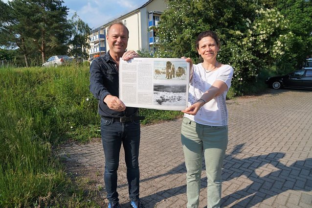 Bild: im Sch&auml;fer und Christina Zyrus stehen an der Ecke Schulstra&szlig;e/Bahnhofstra&szlig;e in Niedersachswerfen, an der die Tafel aufgestellt werden soll. In den H&auml;nden halten sie das Buch Niedersachwerfen von Hilmar R&ouml;mer. Darin ist ein Foto von der Fundsituation am Kohnstein abgebildet.