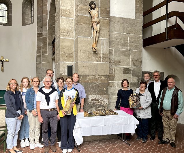 Bild: Die Gemeinde freut sich, das Kruzifix wieder in der Kirche zu wissen. B&auml;rbel Treutler vom Gemeindekirchenrat h&auml;lt die restaurierte Altartafel in H&auml;nden, die damals ebenfalls zerbrochen ist. Pfarrer Klemens M&uuml;ller (im Anzug) steht rechts neben ihr. Den Vorsitzenden des Gemeindekirchenrates, Ralf Schumann, finden Sie links neben dem Tisch, hinten im hellblauen Hemd